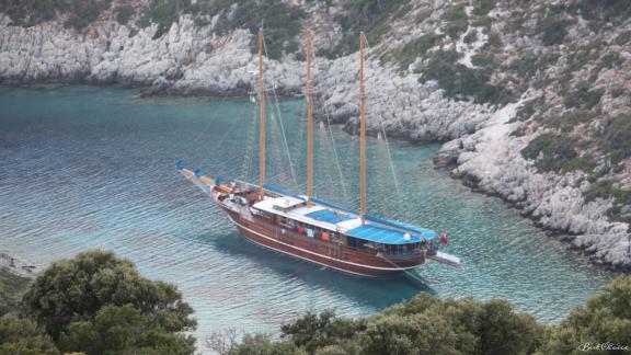 The gulet Bahrieli C with 12 cabins, anchored in a secluded bay with clear water.